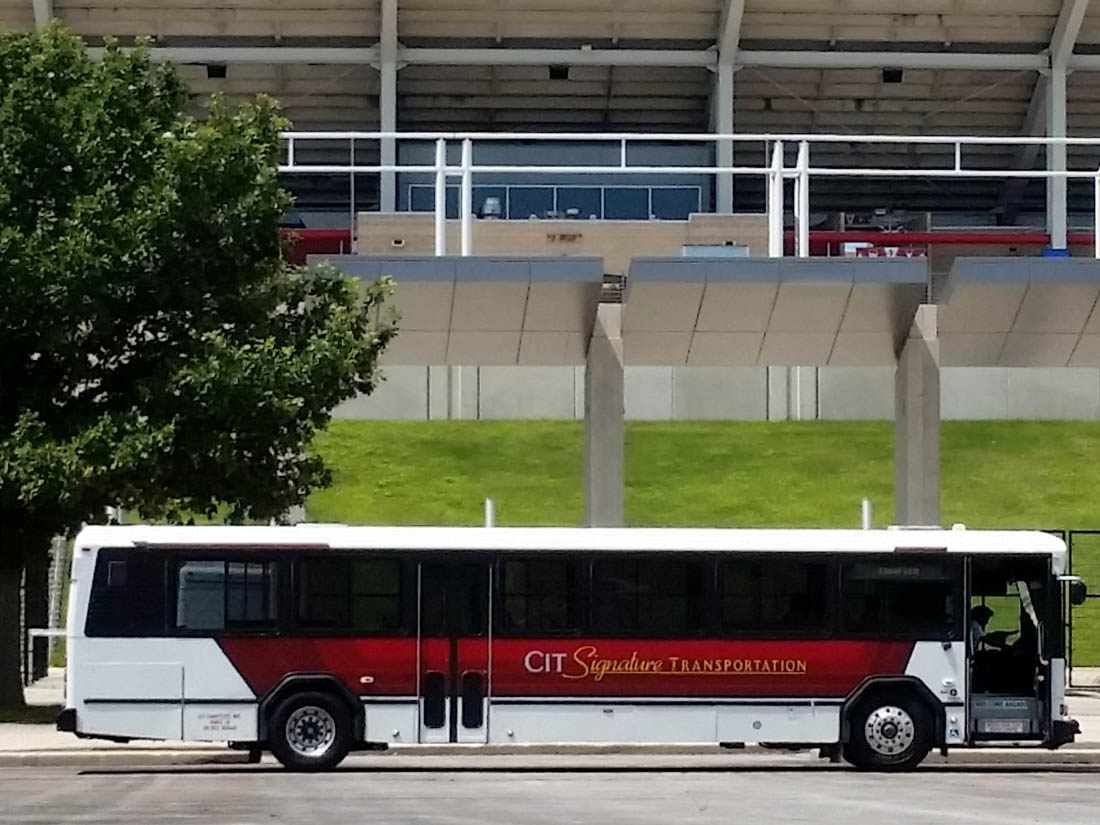 Red and white transit bus at a bus stop in front of a stadium