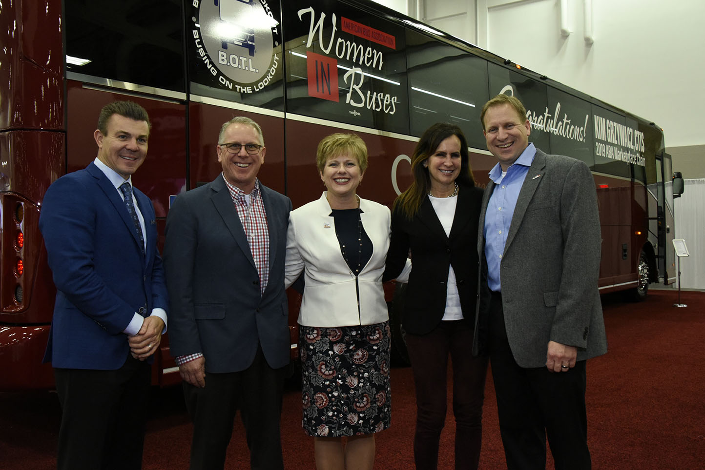 five people dressed in formal attire standing in front of a red CIT coach bus